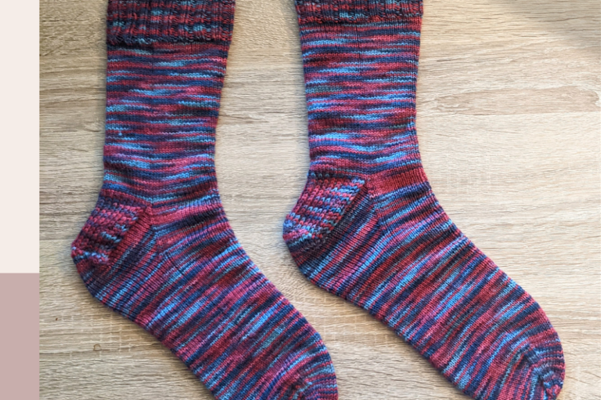 pink blue and purple handknit socks on a light wood background