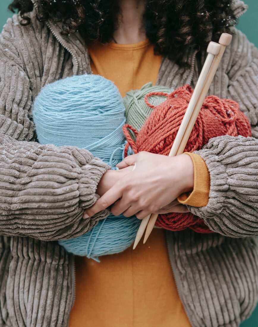 person hugging skeins of yarn and wooden knitting needles