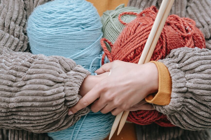 person hugging skeins of yarn and wooden knitting needles