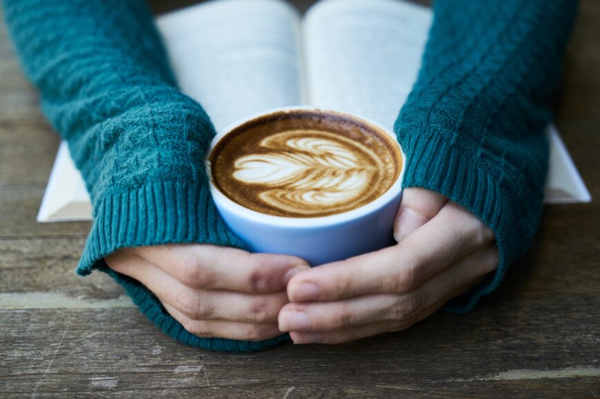 view of woman's hands holding coffee cup and arms holding book open