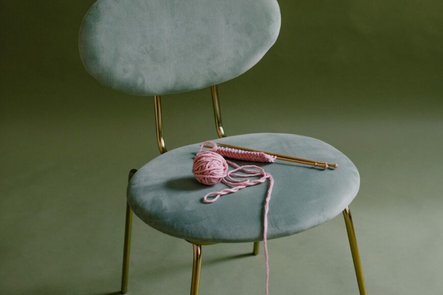 chair with pink yarn and knitting needles sitting on the seat