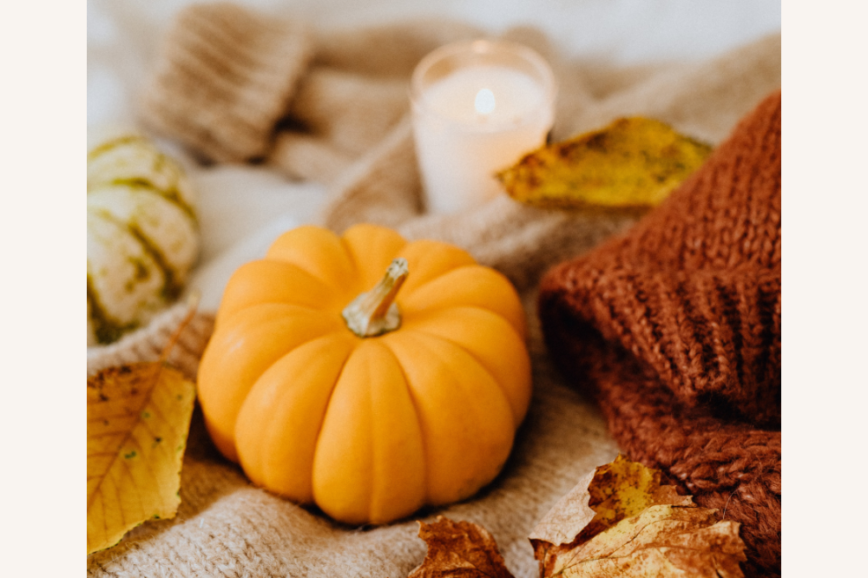 pumpkins with fall leaves and a candle with knitted sweaters on the side